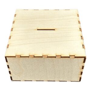 Drewniana skarbonka kuferek ze sklejki o wymiarach 15,5 x 15,5 x 8,6 cm z widocznym otworem na monety i laserowo wycinanymi łączeniami.