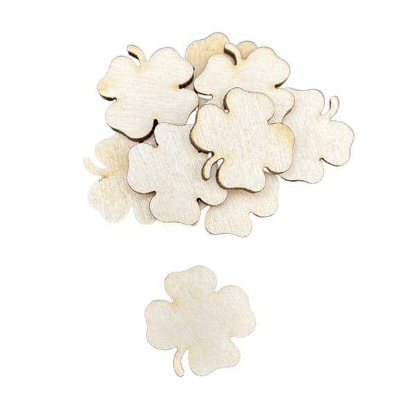 Drewniane Koniczyny Scrapki z Cienka Sklejki 2,5 x 2 cm 10 szt Zestaw drewnianych koniczyn ze sklejki o wymiarach 2,5x2 cm, ułożonych w stos obok pojedynczego elementu.