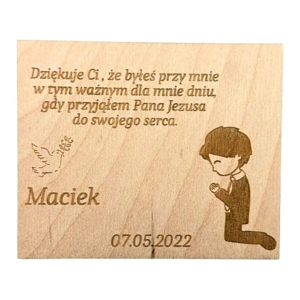 Drewniany magnes personalizowany na komunię ze sklejki o wymiarach 9 x 7,5 cm z grawerem tekstowym, gołębicą i modlącym się chłopcem o imieniu Maciek.