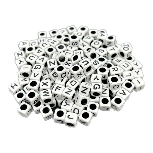 Koraliki z Literkami Białe Kostki DIY 6 mm 25 g Koraliki z literkami białe kostki DIY o rozmiarze 6 mm w opakowaniu 25 g rozsypane na płaskiej powierzchni.
