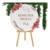 Personalizowana tablica powitalna komunijna koło o średnicy 50 cm z białej płyty HDF umieszczona na drewnianym stojaku.